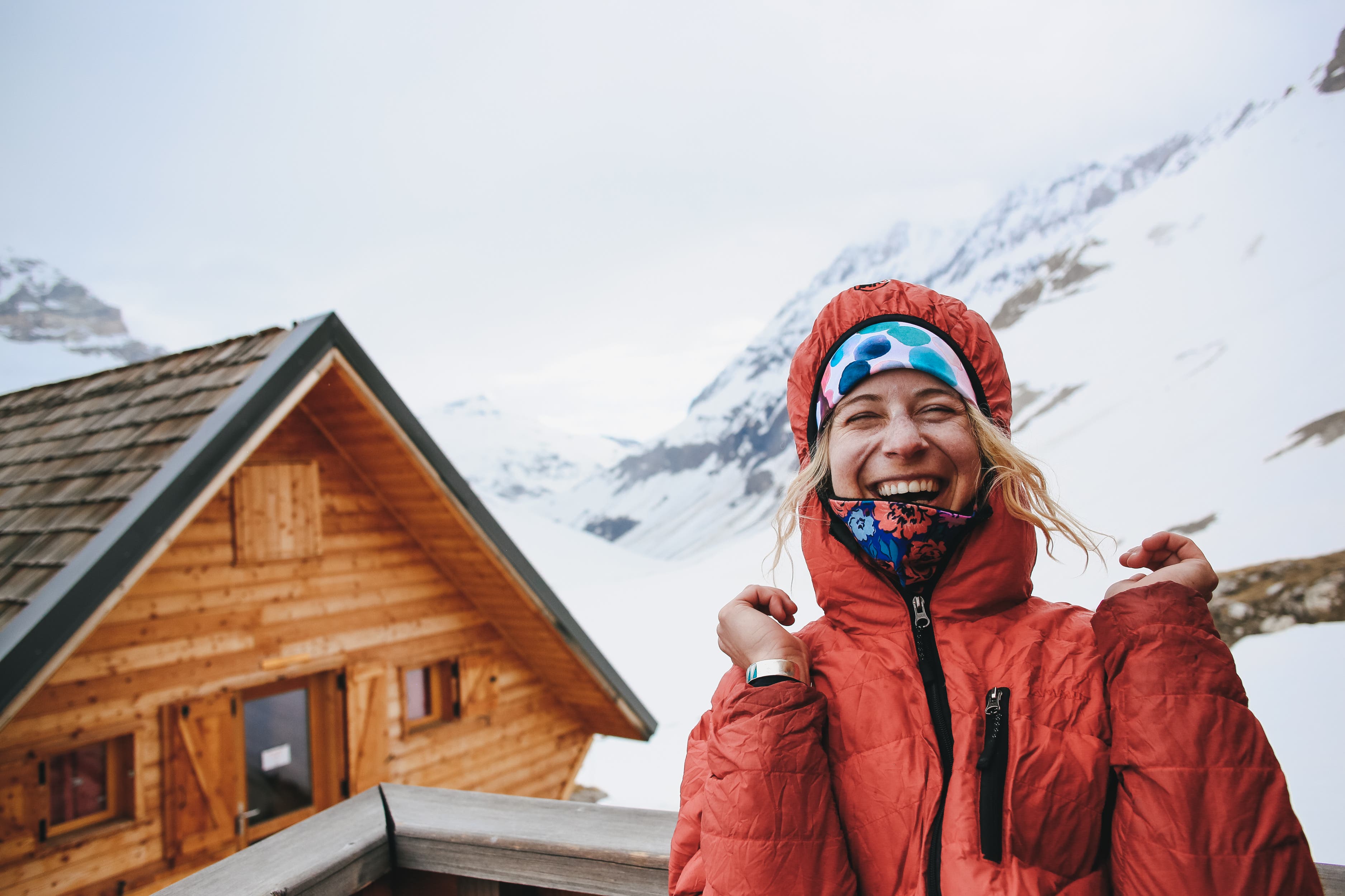 Corinne Prevot laughing in orange snow coat in front of ski cabin in the French Alps