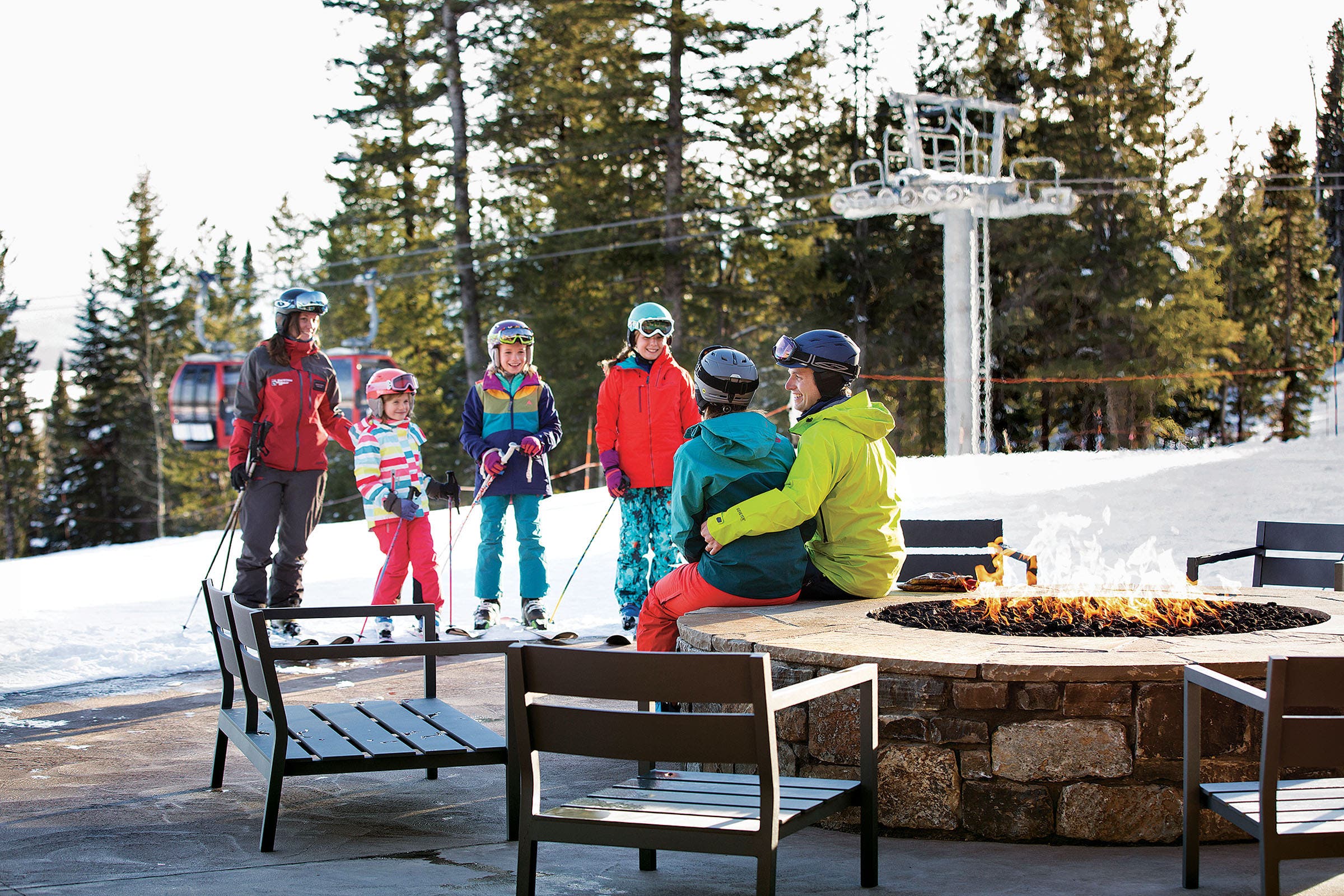 SKI1119-TRA-JHMR-Courtesy4_1 copy Group of skiers young and old in front of large firepit and chairs beside a ski slope and ski lift