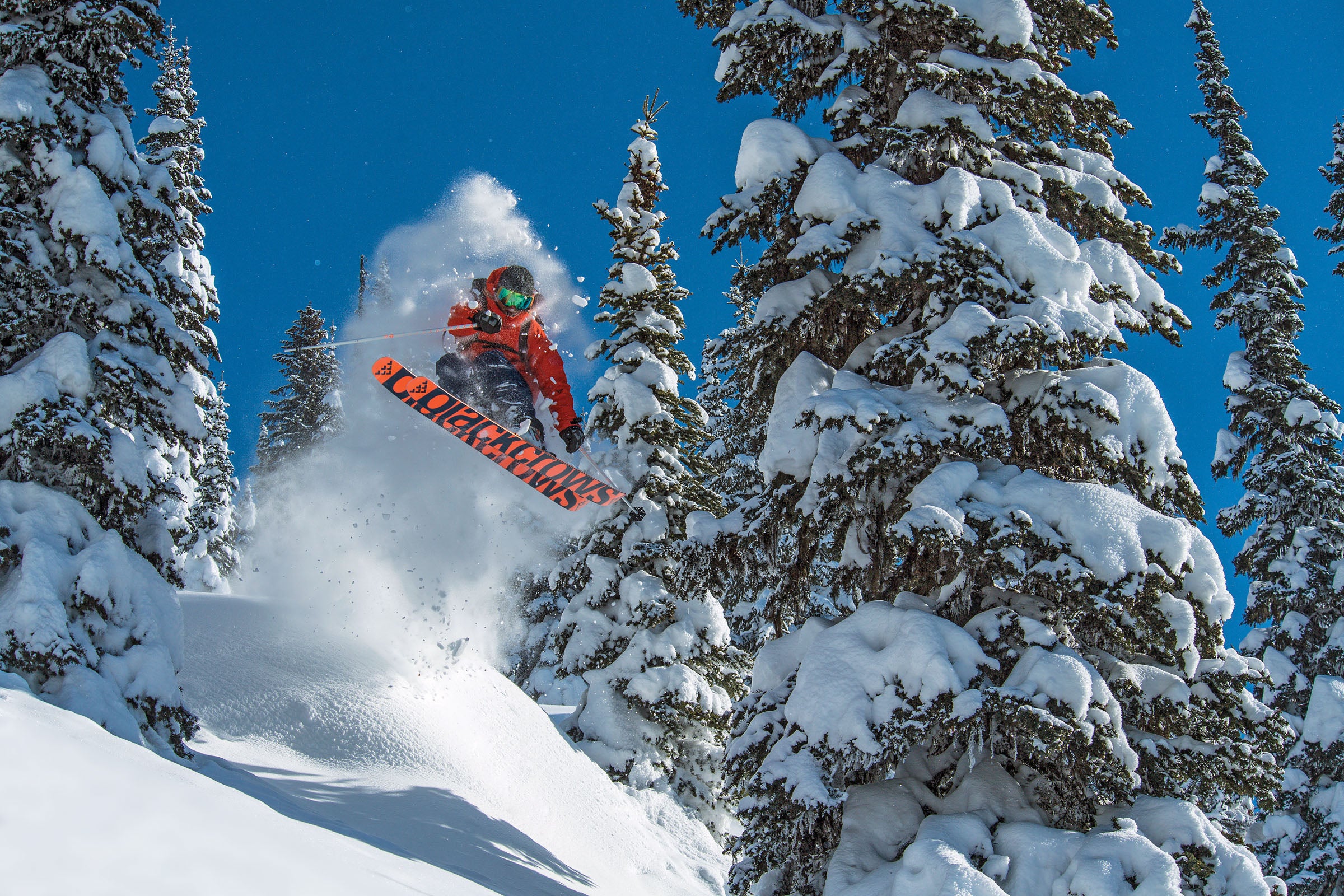 "Mark Abma skiing mid-air through trees with black and red Black Crow skis"