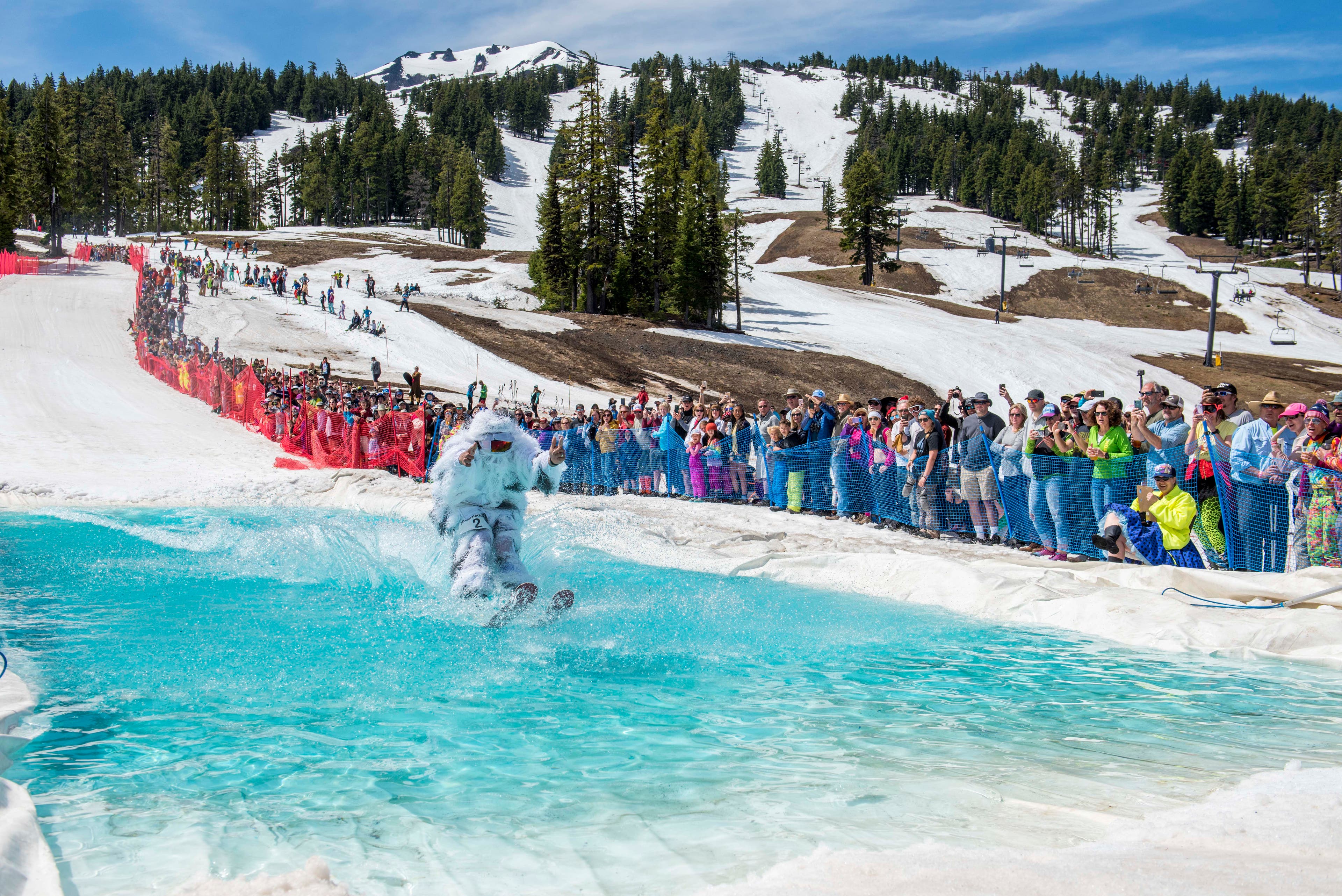 Bachelor052718_AB_098-web_FinaleWeekend Person on white outfit skims a bright blue pond at Mt Bachelor finale weekend while a crowd of people lines the slope.
