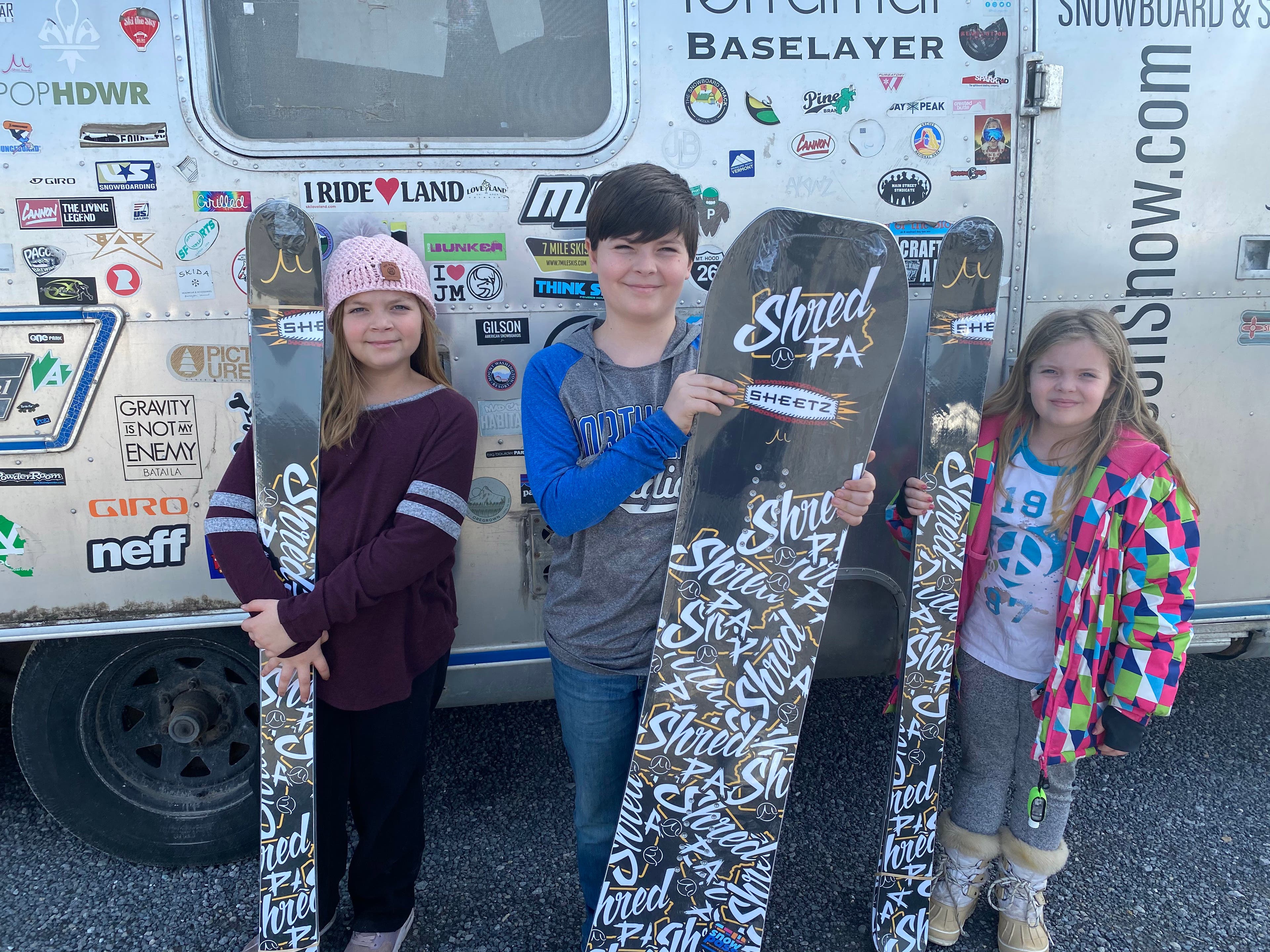 Three participants in the SkiPA 4th and 5th Grade Snowpass Program hold up their free skis and snowboards from Gilson Snow