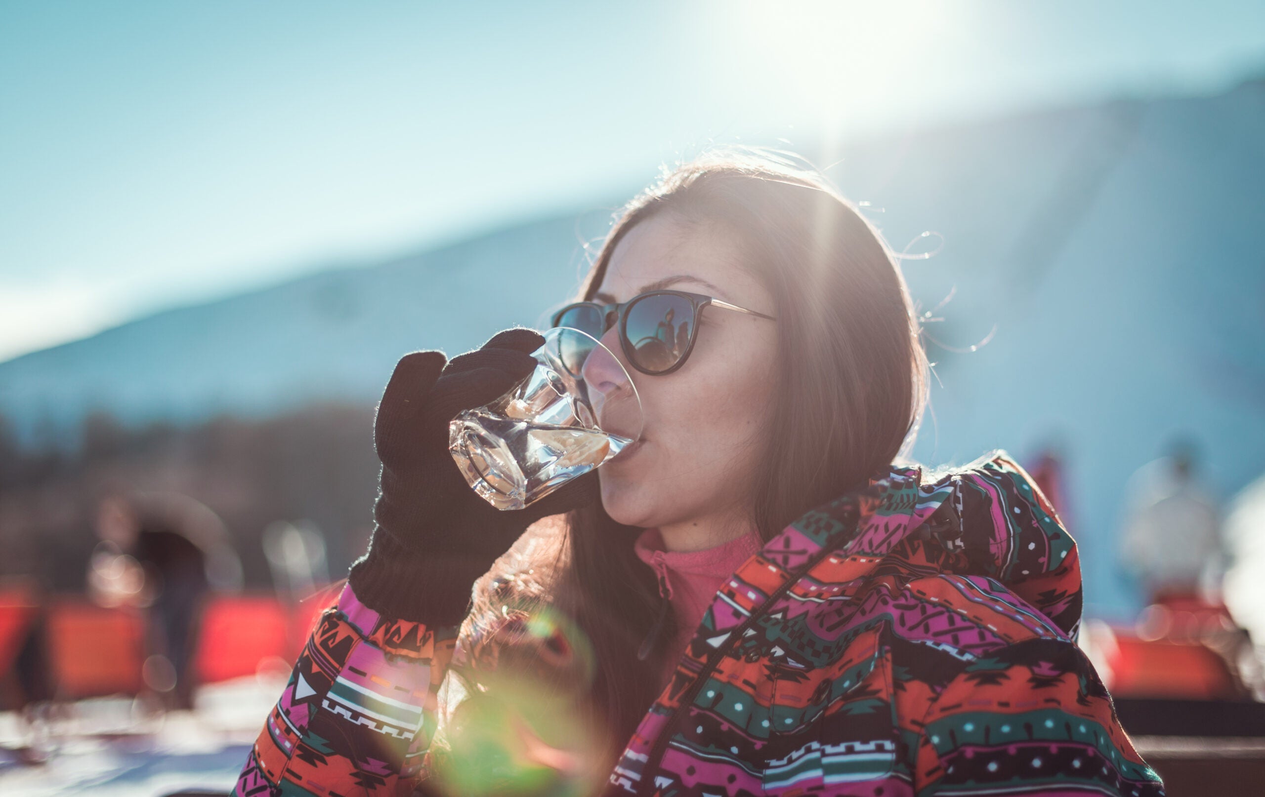 Close-up of a young single woman in a sky-wear drinking cocktail while sitting on a chair at the coffee place in the ski resort
