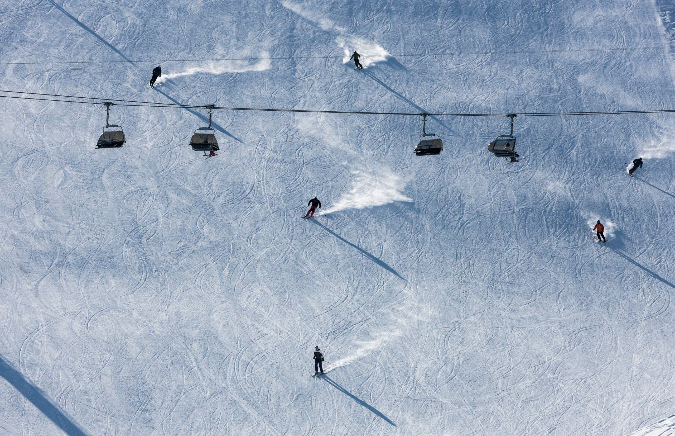 Landscape shot of skiers going down the mountain with a lift overtop