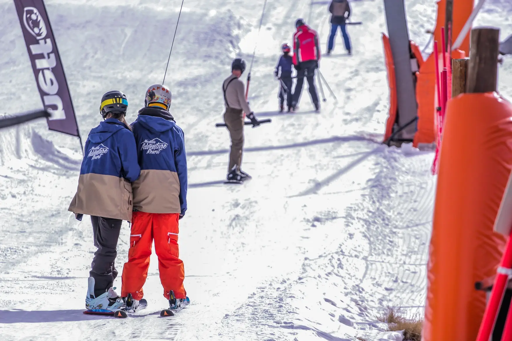 Two young skiers in matching jackets head up a tow rope.