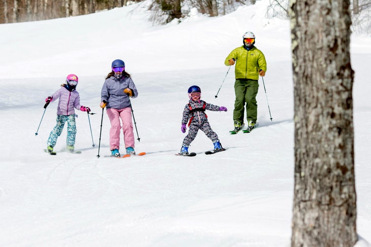 Two adults and two children ski down a mountain.