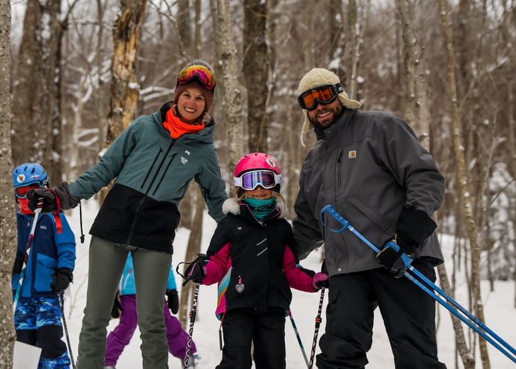 Two adults and a child smile for a photo while skiing through trees