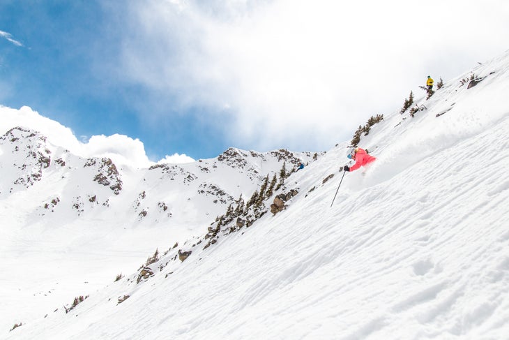 Skier in red heads downward with lots of powder and blue skies