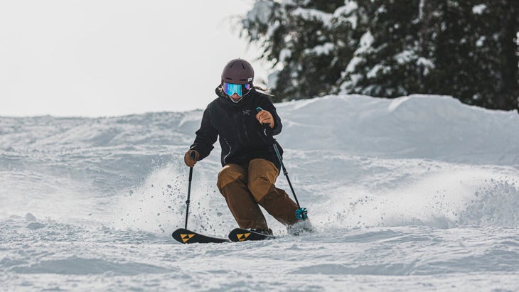 Skier in black jacket and tan pants making a turn in bumps