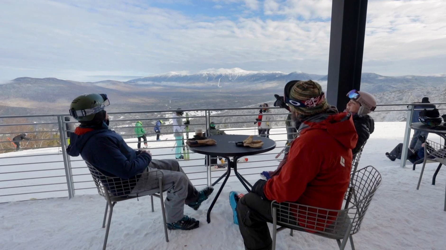 Dua pemain ski duduk di sebuah pondok luar ruangan sambil memandangi pegunungan New Hampshire.