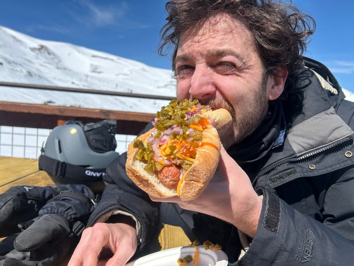 Person eating a hot dog with plenty of toppings 