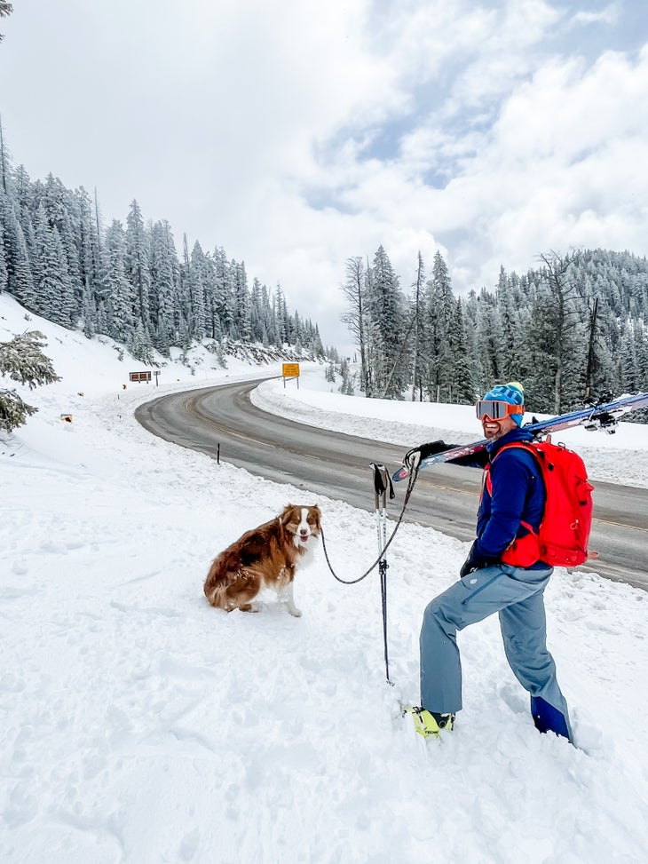 Man with red backpack and skis next to a dog.