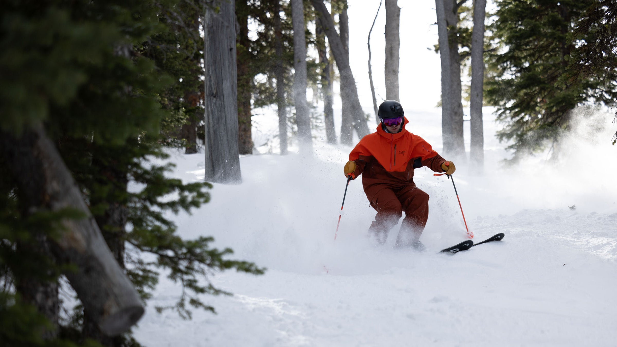 Skier in orange and red jacket skiing through trees at Big Sky