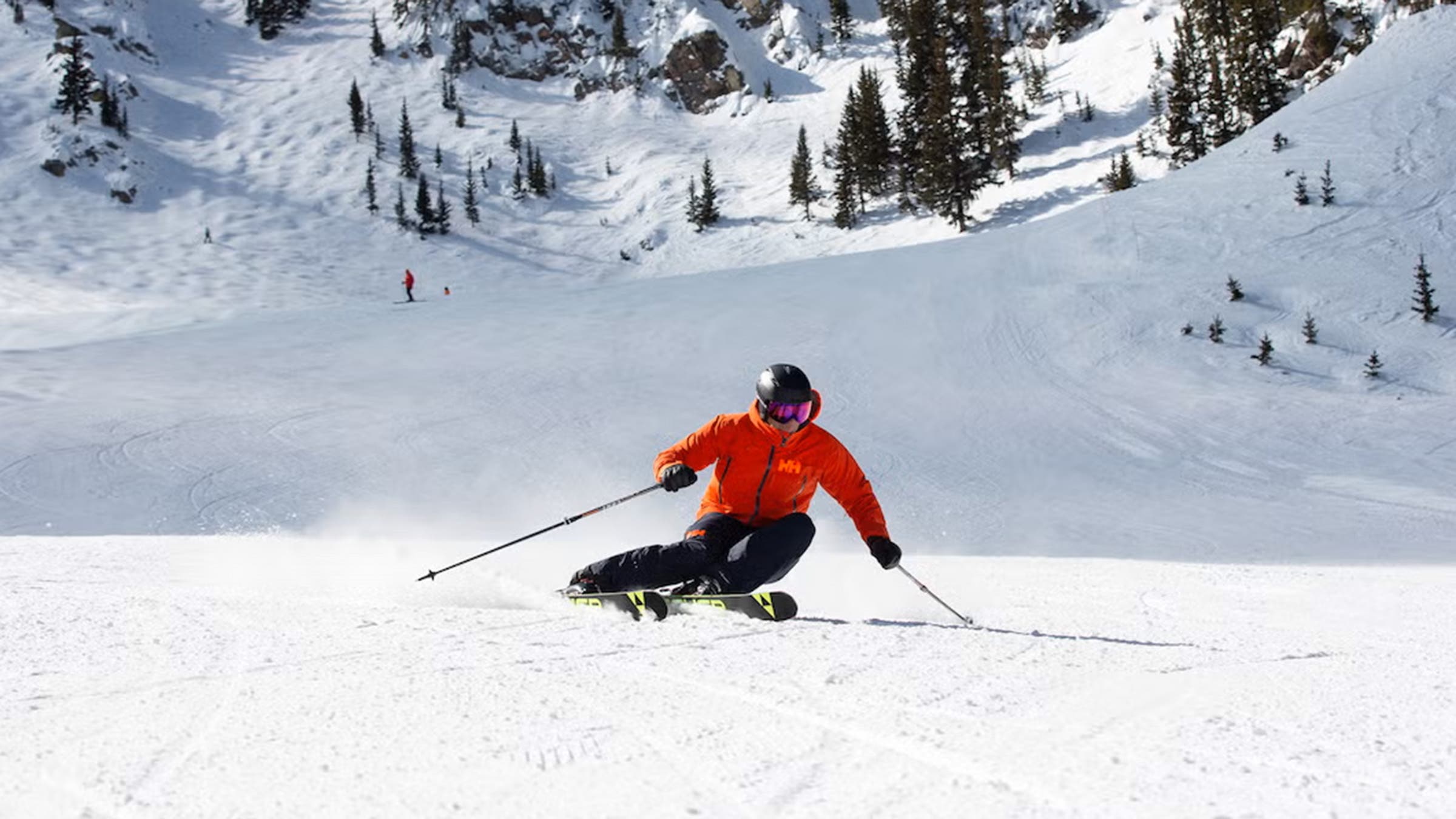Man in red jacket carving down groomed ski slope