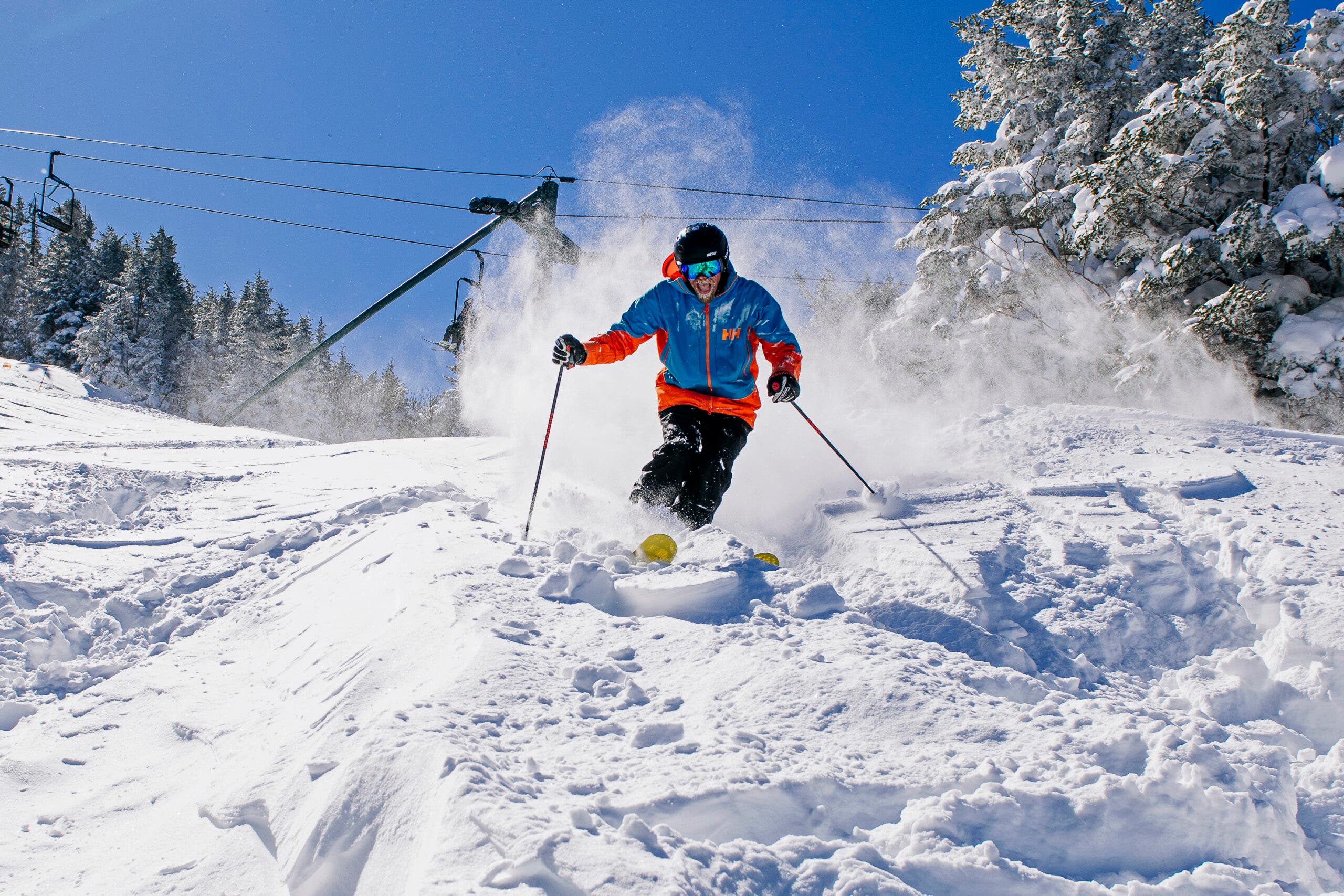 Pemain ski berjaket biru berlari dengan salju