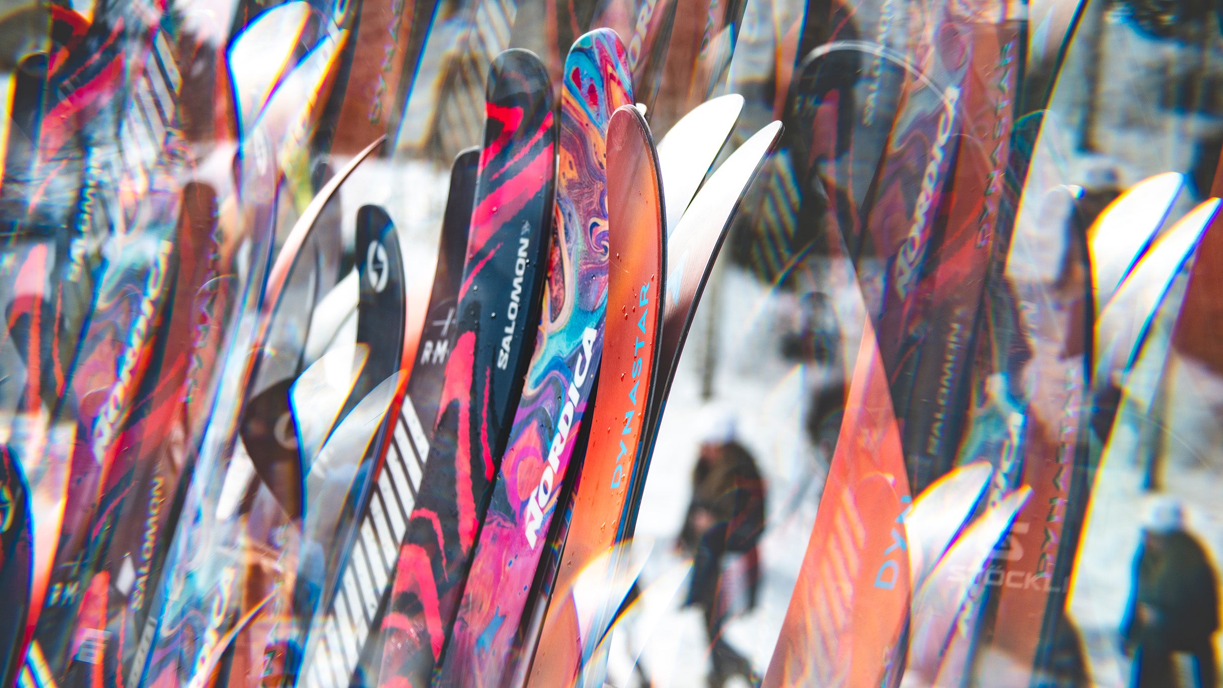 Closeup of dozens of skis leaning on ski rack, only tips showing.