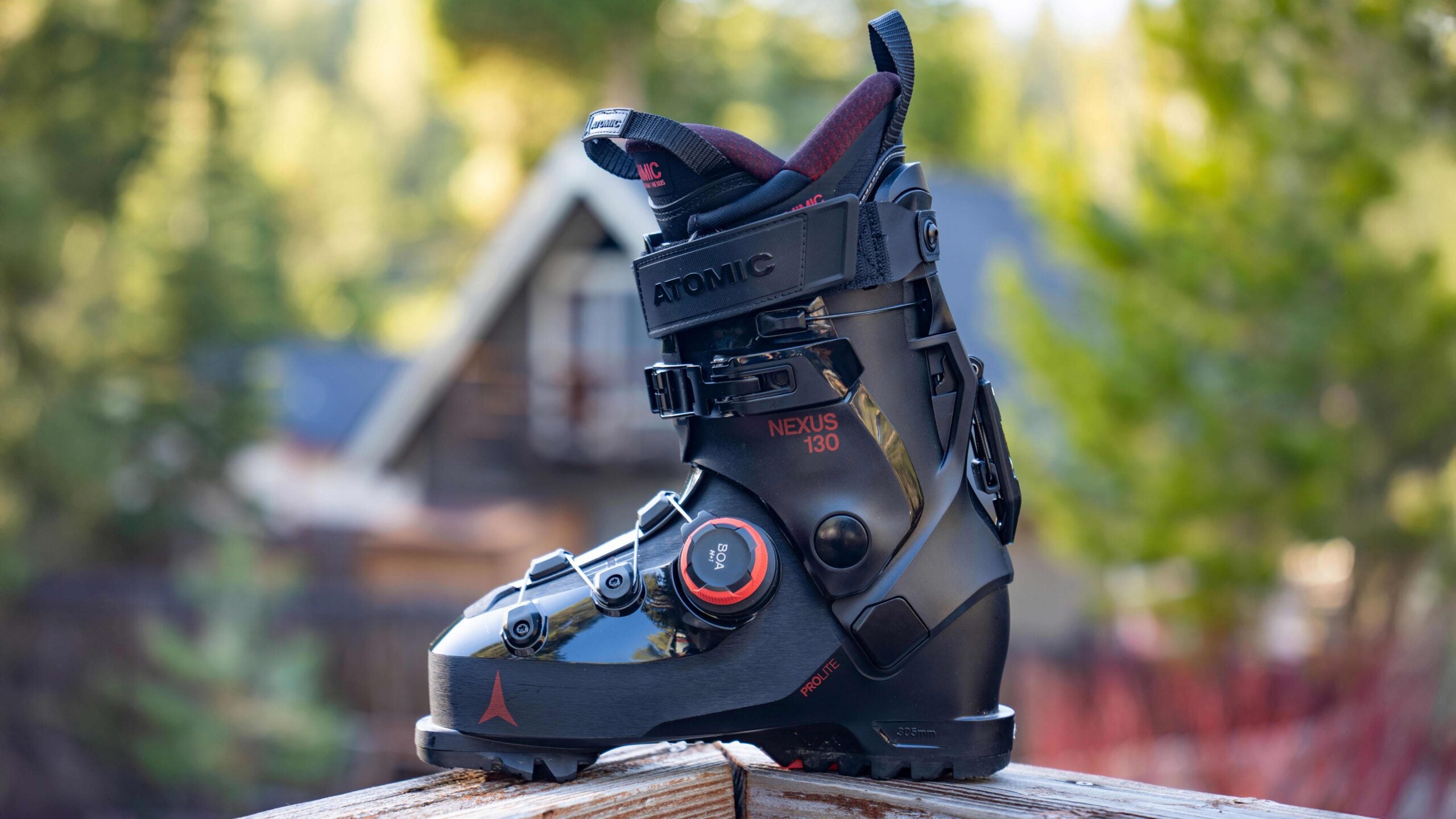 Closeup of black Atomic Nexus 130 BOA ski boot on wooden railing with blurry trees in background