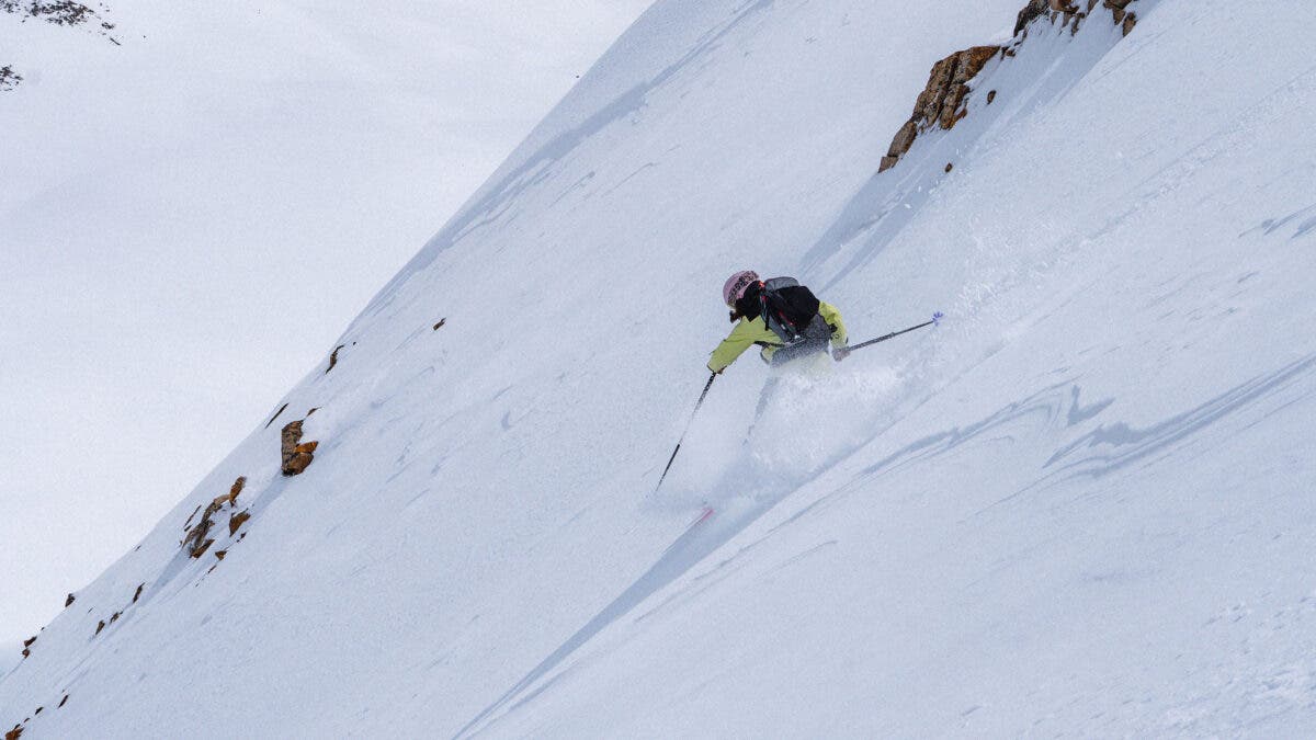 A skier in a yellow jacket makes aggressive turns down a steep snow-covered mountain face above Cooke City, Montana, wearing the Tecnica Zero G Decoy 115 W backcountry ski boots.