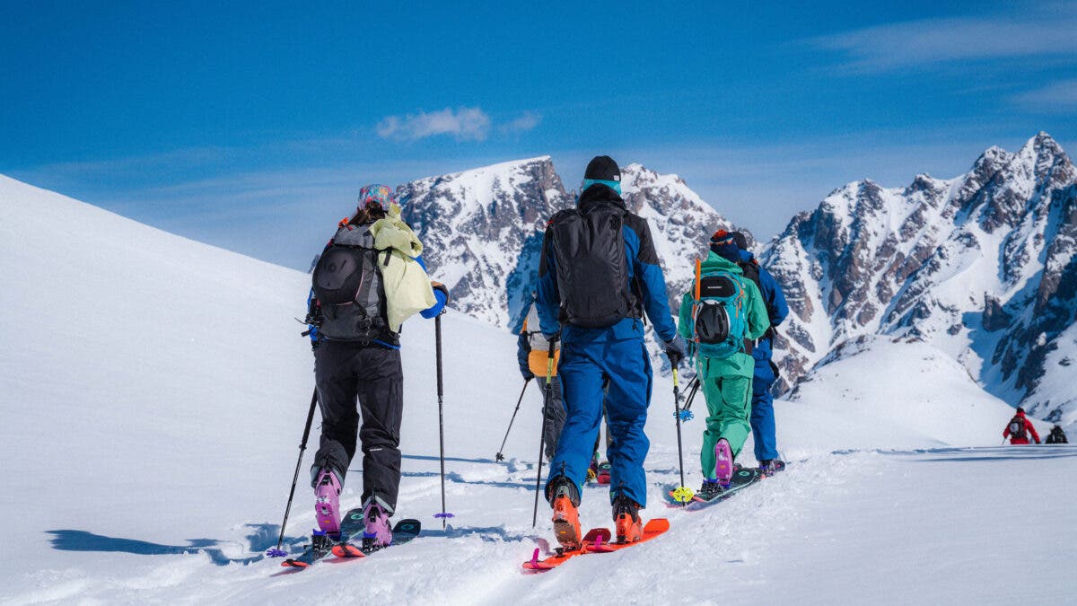 A group of backcountry skiers skinning uphill toward dramatic snow-covered peaks in the Beartooth Mountains above Cooke City, Montana.