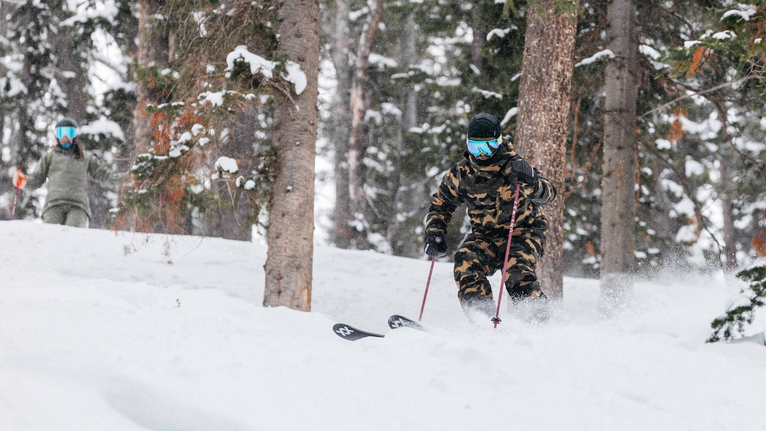 Skier in camouflage ski suit skiing Völkl M7 Mantra through trees during SKI Test