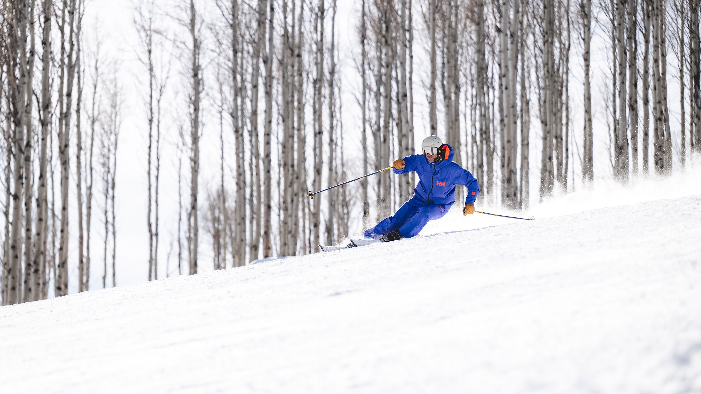 Skier in blue carving on frontside skis with aspens in background