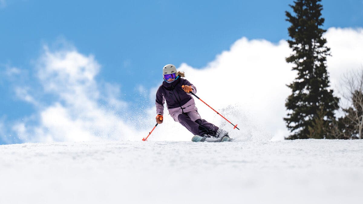 Woman in purple skiing down groomed slope on sunny day