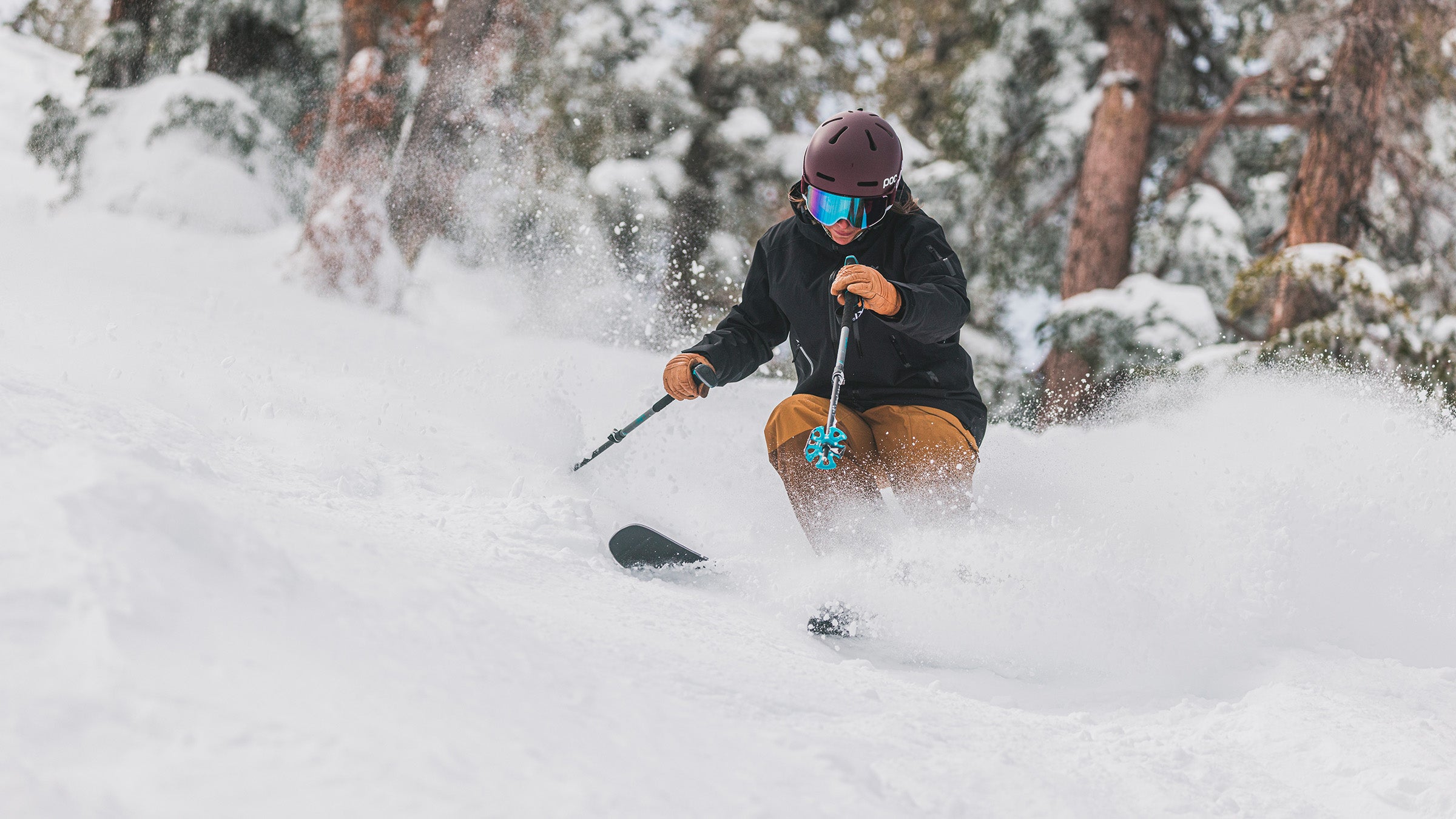 Woman about to pole plant while skiing powder in trees in black shell jacket.