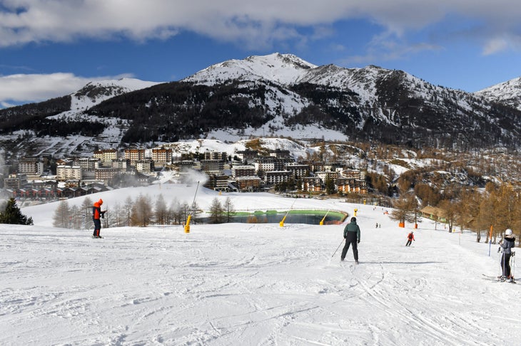 Sestriere, Italy - Jan 16 2025: Skiers and snowboarders descending a ski slope in an Italian ski resort. Wide snowy piste overlooking Sestriere town in the Piedmont region. Winter holiday resort in the mountains